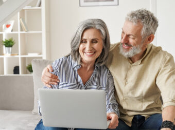 Happy mature mid age couple doing ecommerce shopping using laptop at home.