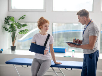Male physiotherapist writing prescriptions, female patient sitting on couch in arm sling