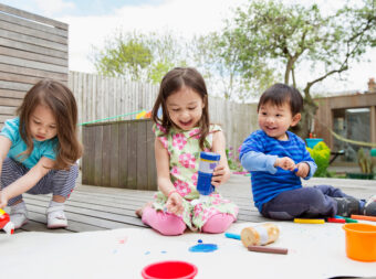 Three young children painting and drawing in garden